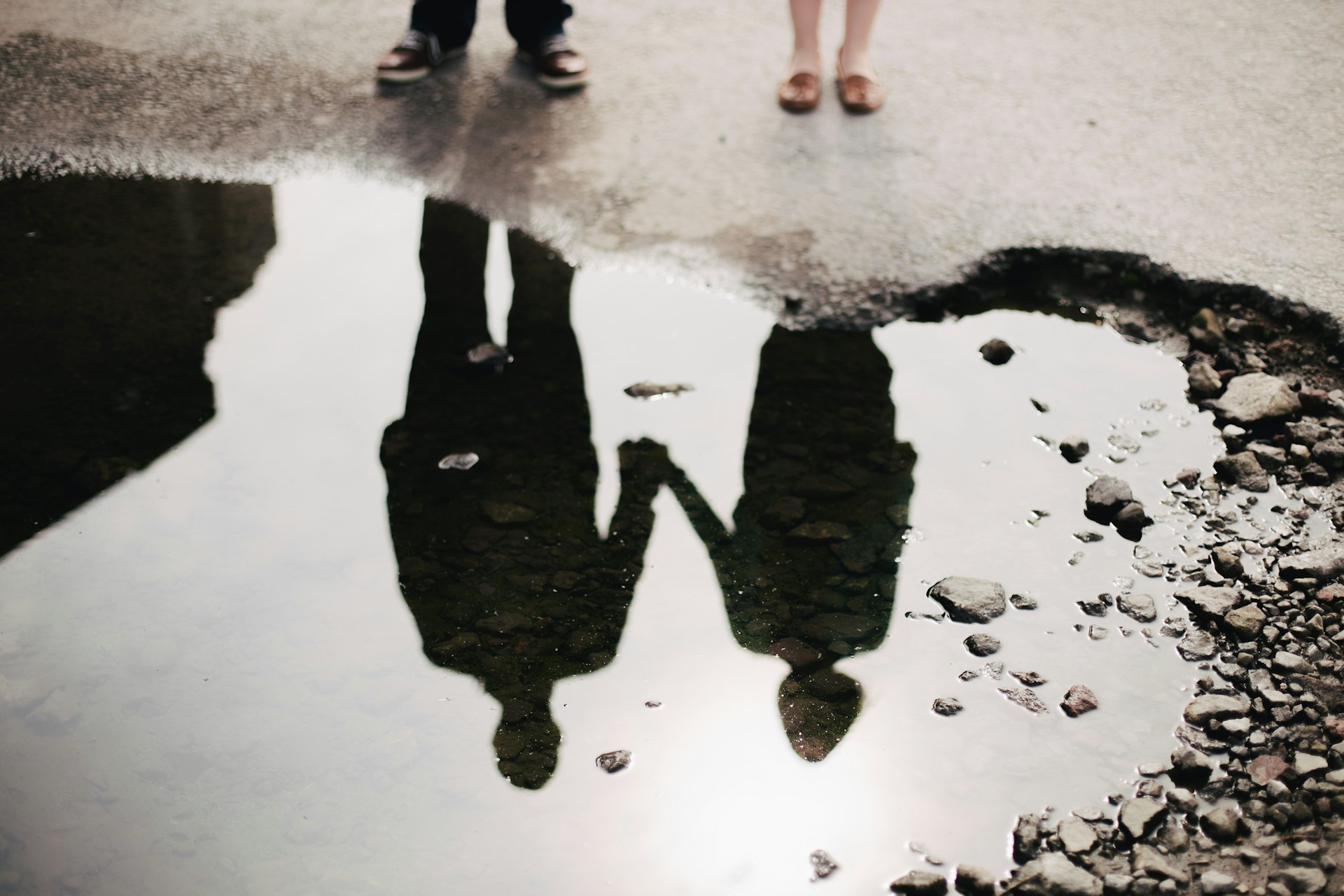 The reflection of two people holding hands is seen in a rain puddle.